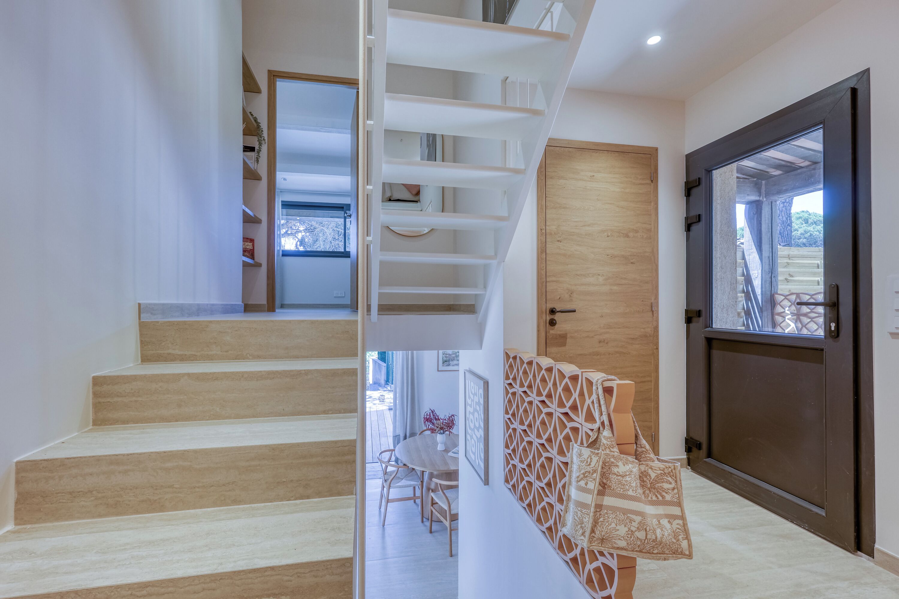 Un intérieur moderne avec un escalier, une porte en bois et une vue à travers une porte vitrée.