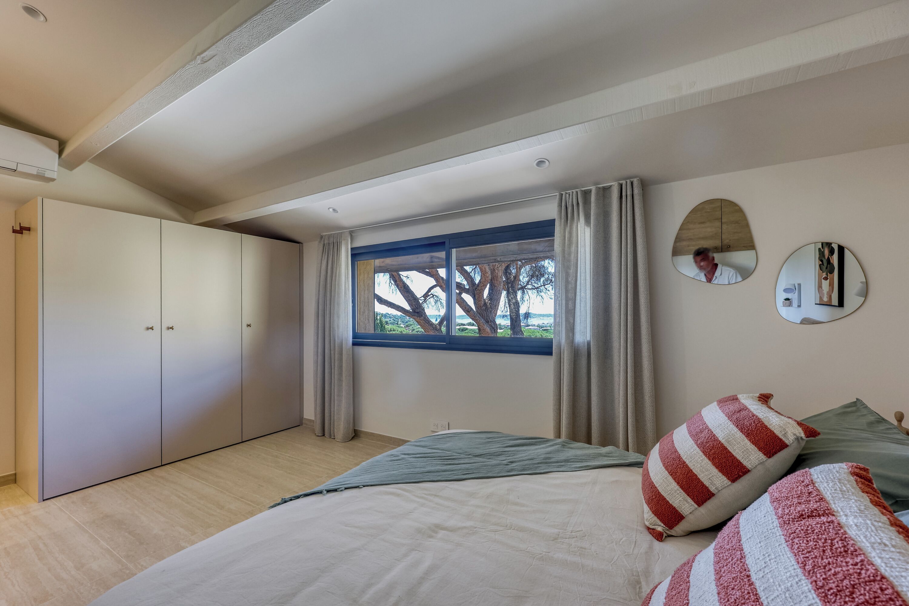 Une chambre à coucher avec un lit, une armoire, une fenêtre avec des rideaux et un miroir sur le mur.