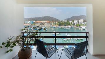 A balcony with a view of a marina, a potted plant, and two chairs.