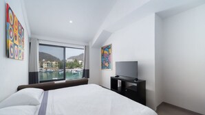 Ein Hotelzimmer mit einem großen Bett, einem Fernseher, einem Fenster mit Blick auf Boote und Gebäude sowie zwei Kunstwerken an den Wänden.