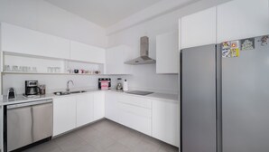 Eine moderne Küche mit weißen Schränken, einem Edelstahlkühlschrank, einer Kaffeemaschine und einem Geschirrspüler.