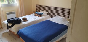 A hotel room with two beds, a suitcase, a hat, and a radiator. - House with a garden (fenced), in a very quiet area, with a view of the forest (Lacanau)