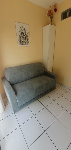 A grey sofa, a white cabinet, and a framed picture on a yellow wall. - House with a garden (fenced), in a very quiet area, with a view of the forest (Lacanau)