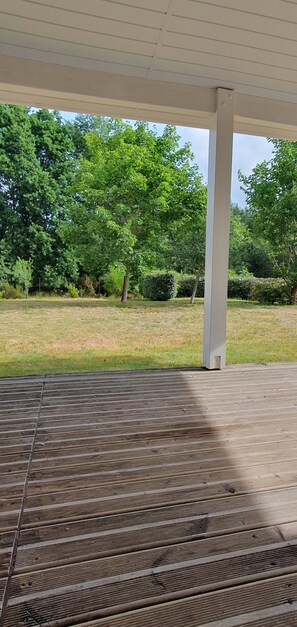 A covered outdoor area with a wooden deck, surrounded by trees and a grassy lawn. - House with a garden (fenced), in a very quiet area, with a view of the forest (Lacanau)