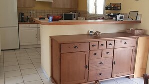 Keittiössä on keskellä sijaitseva saareke, puukehikot, valkoinen jääkaappi ja seinällä oleva kello.