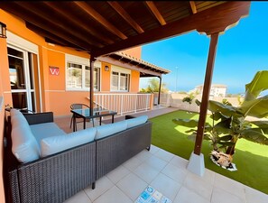 Une terrasse extérieure avec un canapé en osier, une table et une chaise.