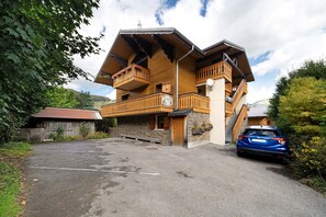 Ein mehrstöckiges Holzgebäude mit Balkonen und einem Steinfundament, davor ein geparktes Auto.