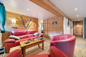 Ett mysigt vardagsrum med en röd lädersoffa, ett träbord och skidor och snowboards som hänger på väggen.