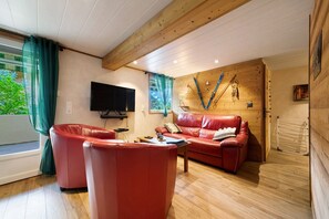 Ein gemütliches Wohnzimmer mit einem roten Ledersofa, einem Flachbildfernseher und Holzwänden.