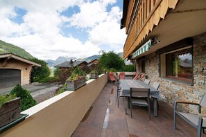 Eine Terrasse mit Tisch und Stühlen, umgeben von Steinmauern und Blick auf Berge.