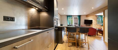 Una cocina moderna con horno empotrado, una barra con taburetes y una zona de comedor con sofá rojo.