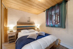 A bedroom with a wooden ceiling, a bed with white bedding, a nightstand with a lamp, and a window with curtains. - Apartment for 7 Guests – Châtel – Terrace, Parking, Near the Slopes (Châtel)