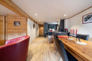 Eine moderne Küche mit Holzschränken, ein Essbereich mit Holztisch und -stühlen sowie ein rotes Ledersofa.