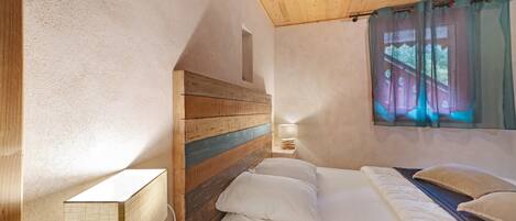 A bedroom with a wooden headboard, a bedside table with a lamp, and a window with curtains.