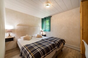 Ein Schlafzimmer mit einem Bett, Nachttischen, einer Lampe, einem Fenster mit Vorhängen und einem Holzschrank.