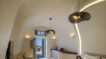 Un dormitorio moderno y bien iluminado con una cama grande, una zona de estar con una mesa, una cocina con mostrador y vistas a través de una puerta abierta.