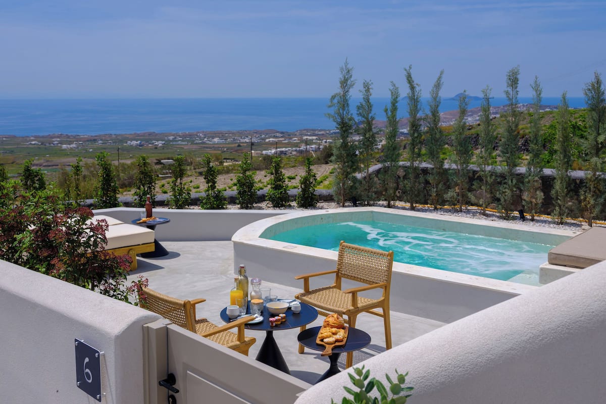Zona junto a la piscina con vista al mar, una mesa con alimentos para el desayuno y una silla de mimbre.