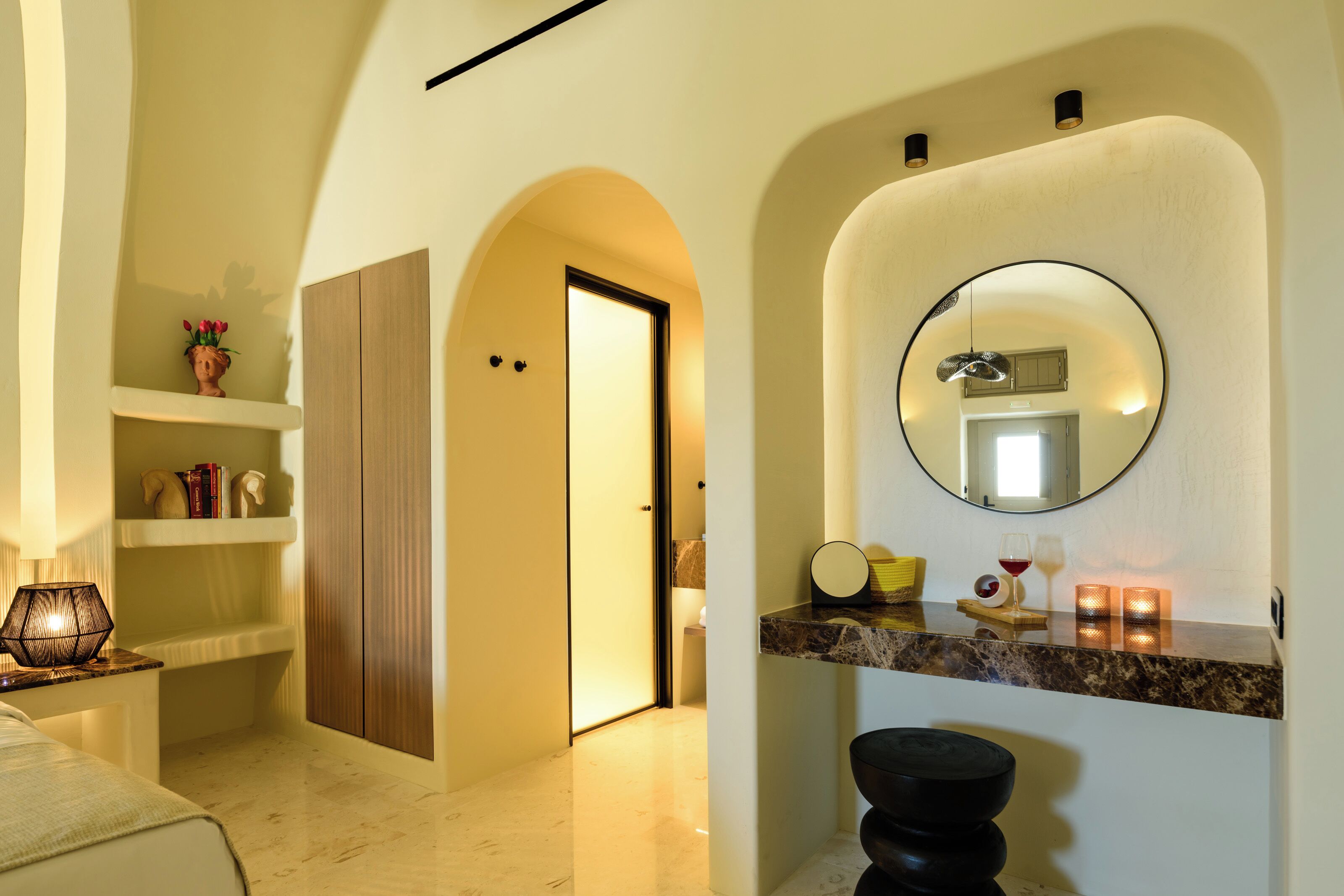 A modern bathroom with a marble countertop, a round mirror, and a shelf with decorative items.