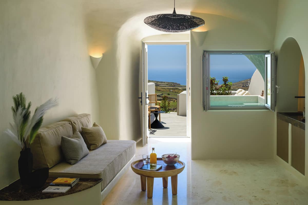 Una sala de estar moderna con un sofá, una mesita con una bebida y vista al mar a través de una puerta abierta.
