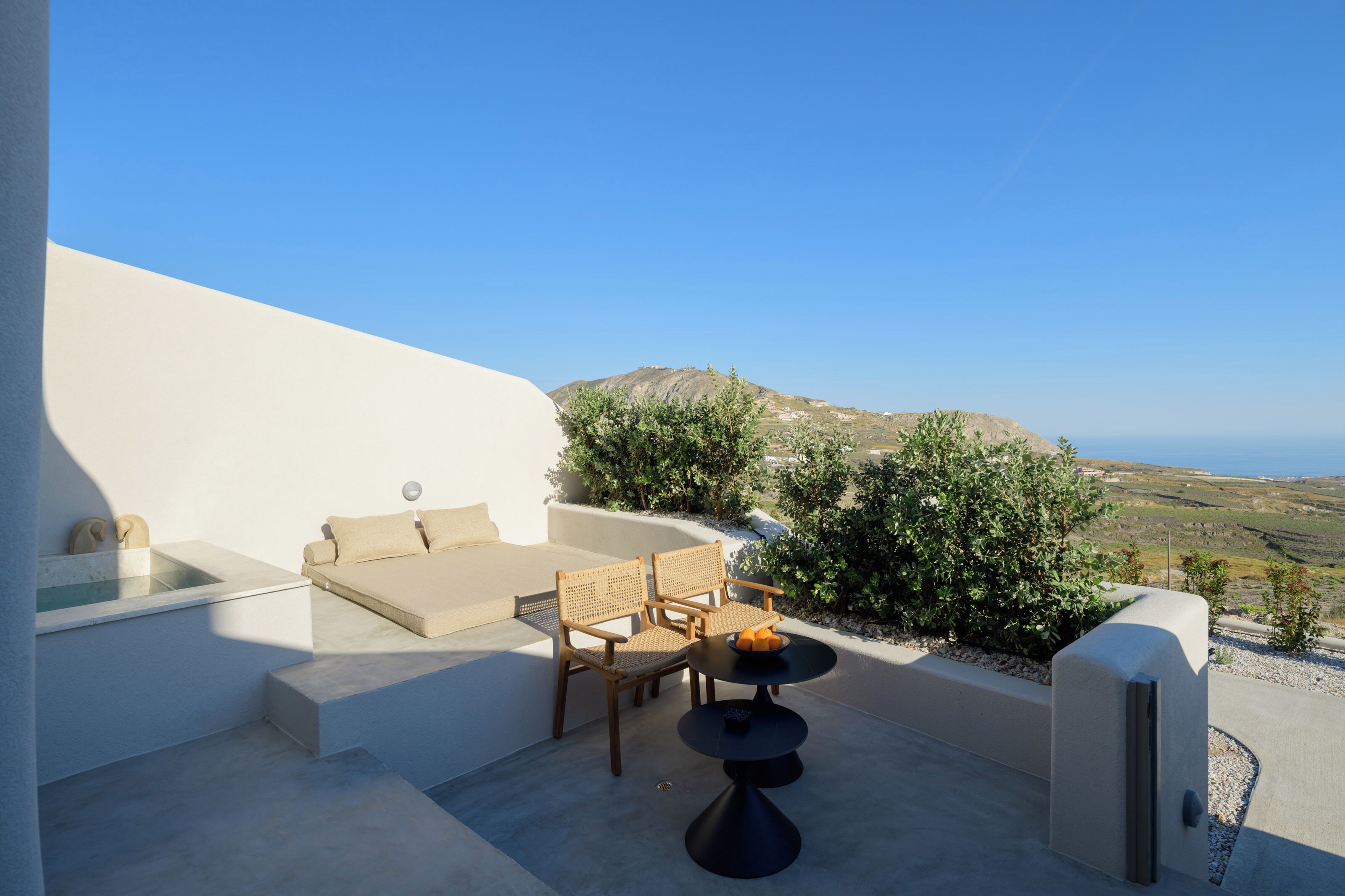 Une terrasse avec un canapé, des chaises et une table, offrant une vue sur un paysage vallonné et un ciel dégagé.