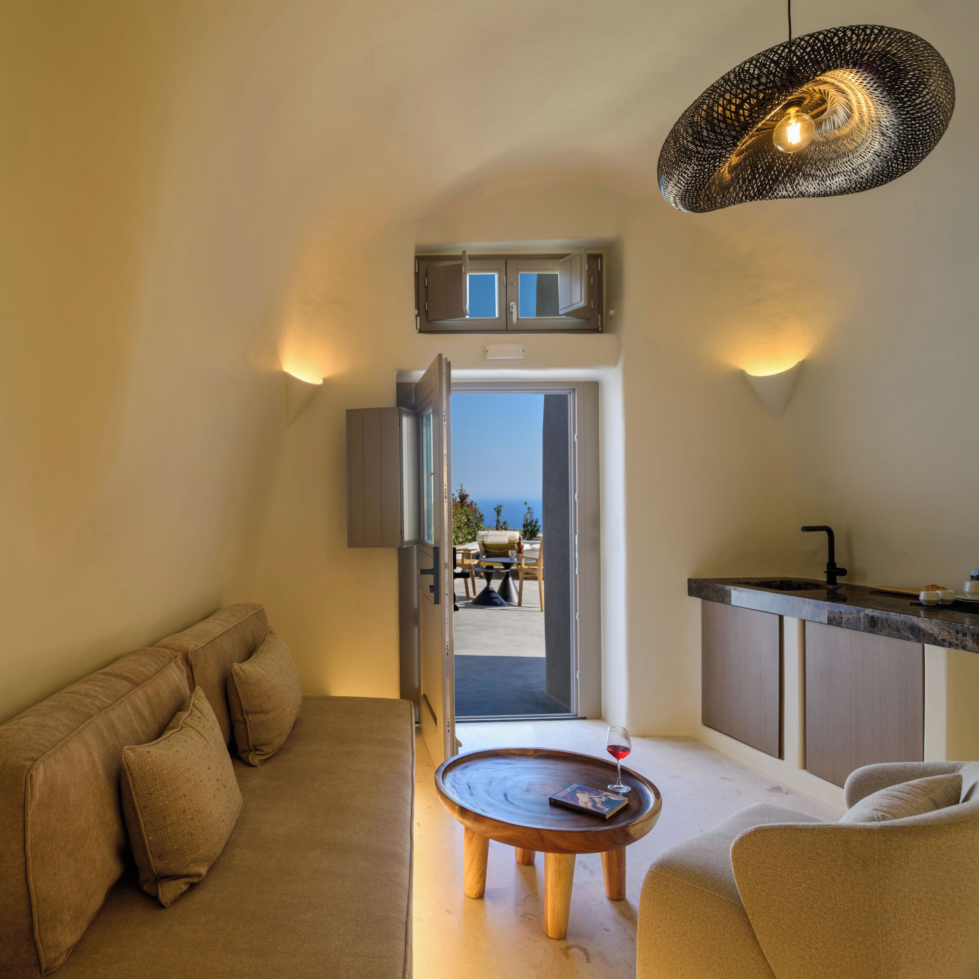 A modern living room with a sofa, a coffee table, and a view of the sea through an open door.