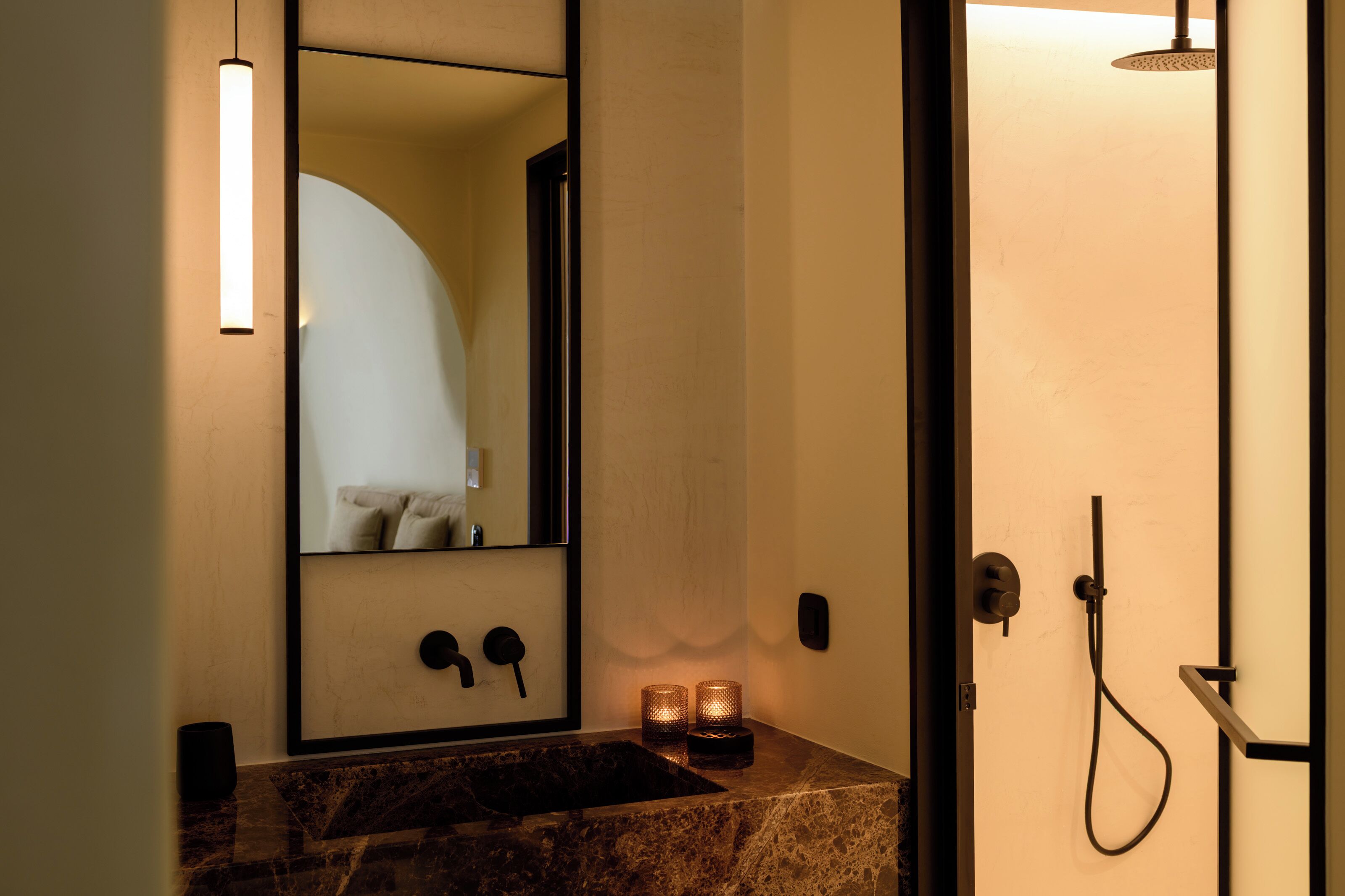 A bathroom with a marble sink, a mirror, a shower, and two lit candles.