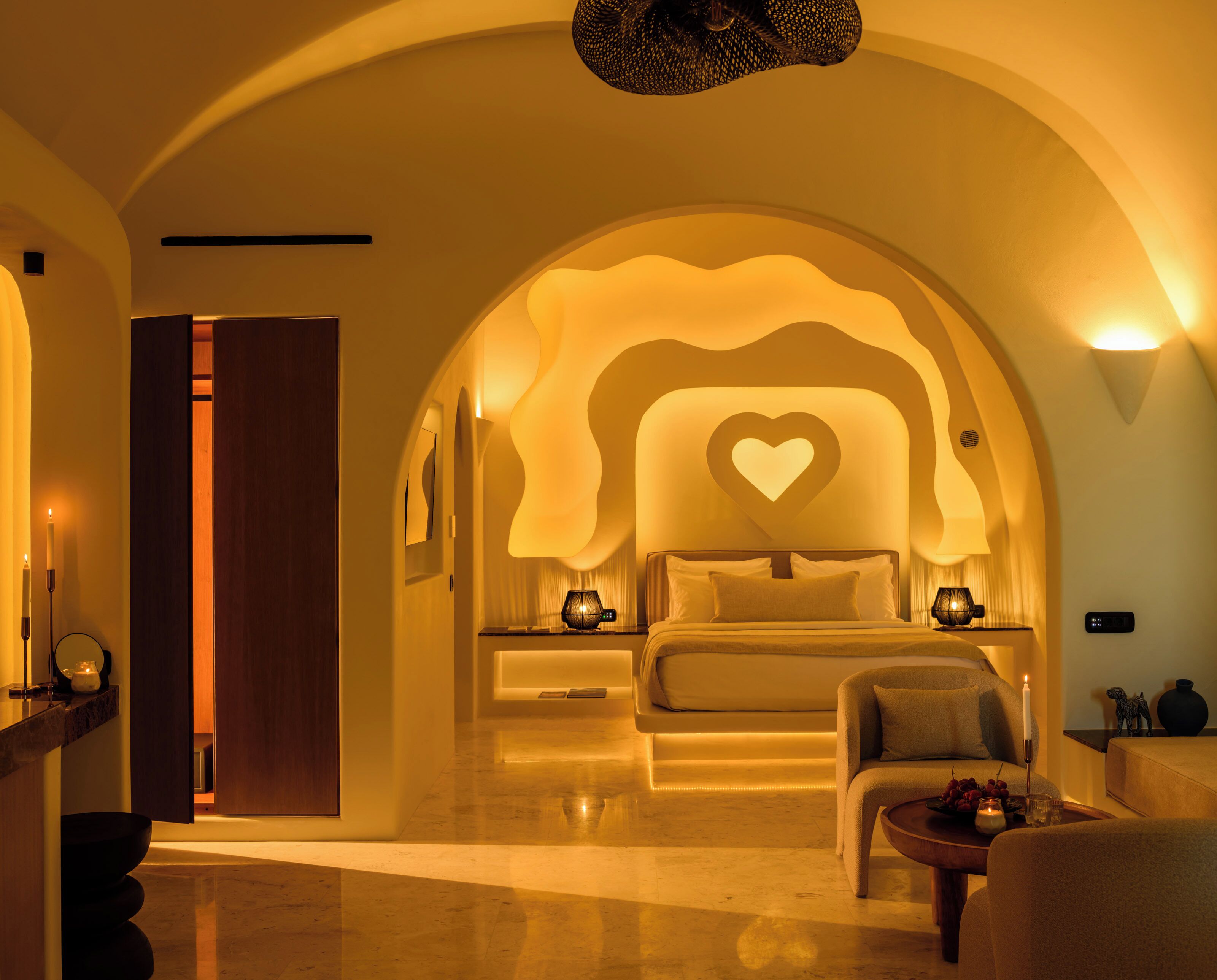 A hotel room with a bed, a chair, a table, and a decorative heart-shaped light on the wall.