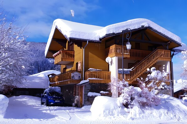 Un chalet en bois dotĂ© dâun balcon, dâun escalier et dâune voiture garĂ©e devant.