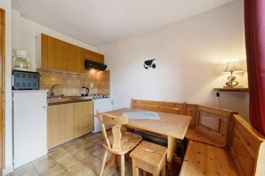A compact kitchen with wooden cabinets, a small dining table, and a single chair. - 2-Room Apartment for 4 – Châtel – Balcony, Parking, Near the Slopes (Châtel)