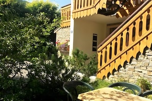 A building with a stone facade, a wooden balcony with a patterned railing, and a small table with chairs in the foreground. - 2-Room Apartment for 4 – Châtel – Balcony, Parking, Near the Slopes (Châtel)