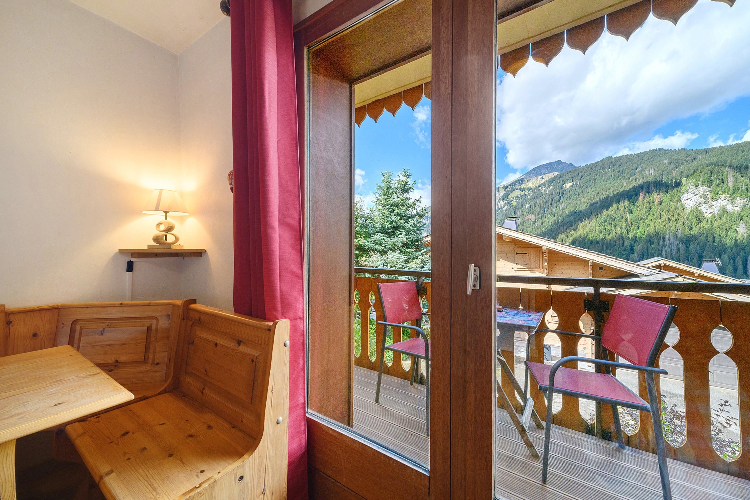 A wooden bench and a table in a room with a view of a mountain landscape.
