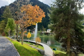 A pathway leading to a lake with a fountain, surrounded by trees and houses. - 2-Room Apartment for 4 – Châtel – Balcony, Parking, Near the Slopes (Châtel)