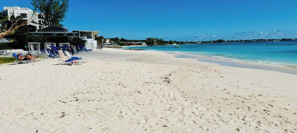 A beach with white sand, lounge chairs, and a building in the background. - Tropical Oasis with Pool & Outdoor Dining Near Beaches & Oistins Fish Fry (Oistins)