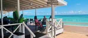 A covered outdoor seating area with chairs and tables, overlooking a turquoise sea. - Tropical Oasis with Pool & Outdoor Dining Near Beaches & Oistins Fish Fry (Oistins)