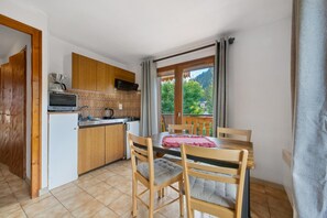 A compact kitchen with wooden cabinets, a built-in oven, and a dining area with a table and chairs. - Apartment for 5 in Châtel – Near Slopes, Balcony, Free Private Parking (Châtel)