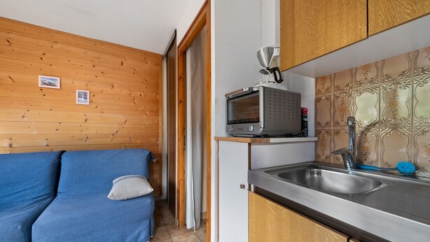 Eine kompakte Küche mit Holzausstattung, einer eingebauten Mikrowelle und einem Spülbecken.