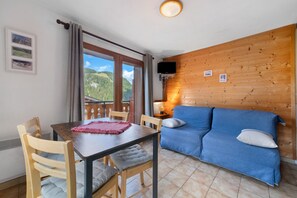 Ett rum med en vägg av trä, en blå soffa, ett bord med stolar och en utsikt över ett bergigt landskap genom ett fönster.