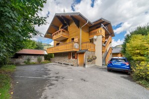 A multi-story wooden chalet with balconies, a stone facade, and a parking area. - Apartment for 5 in Châtel – Near Slopes, Balcony, Free Private Parking (Châtel)