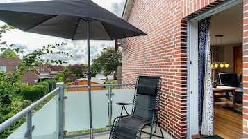 Ein Balkon mit Stuhl, Sonnenschirm und Blick auf ein Backsteingebäude.