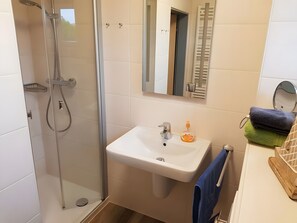 Ein Badezimmer mit einer gläsernen Duschkabine, einem weißen Waschbecken mit Spiegel darüber und einem Handtuchhalter mit Handtüchern.