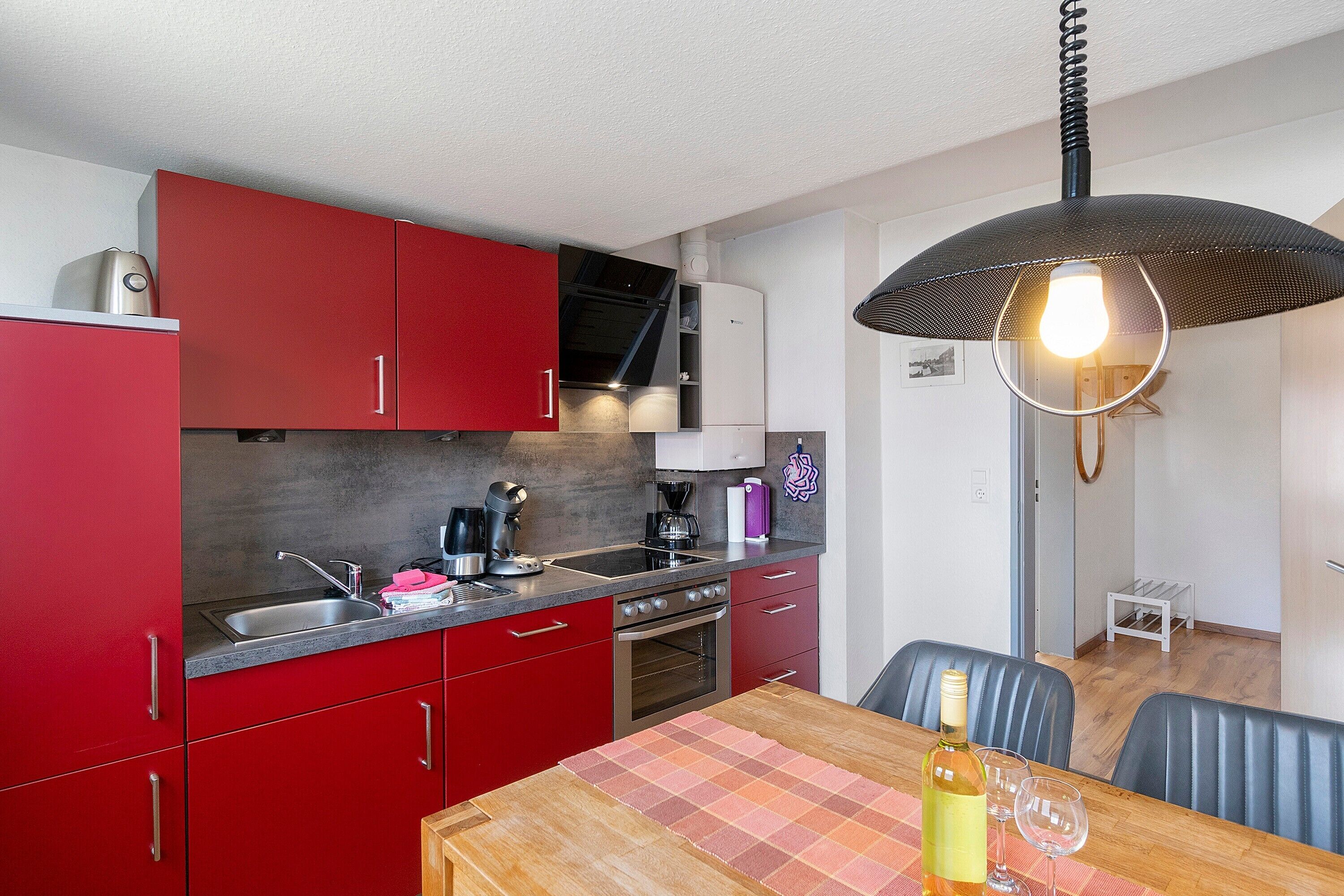 Une cuisine compacte avec des meubles rouges, un évier en acier inoxydable et un luminaire suspendu moderne.