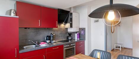 Une cuisine compacte avec des meubles rouges, un évier en acier inoxydable et un luminaire suspendu moderne.