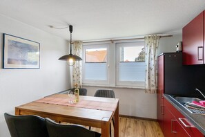 Een kleine keuken met een eettafel, stoelen, een hanglamp en een raam met gordijnen.