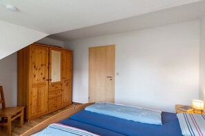 Un dormitori amb un llit, un armari de fusta, una porta i una tauleta de nit amb una làmpada.