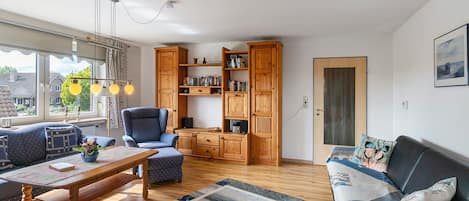 A cozy living room with a sofa, armchair, and a wooden cabinet with books.