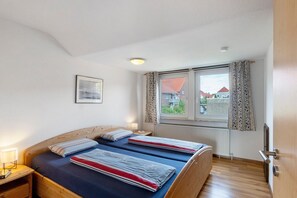 Een slaapkamer met twee bedden, een raam met gordijnen, een radiator en een lijst met een afbeelding aan de muur.