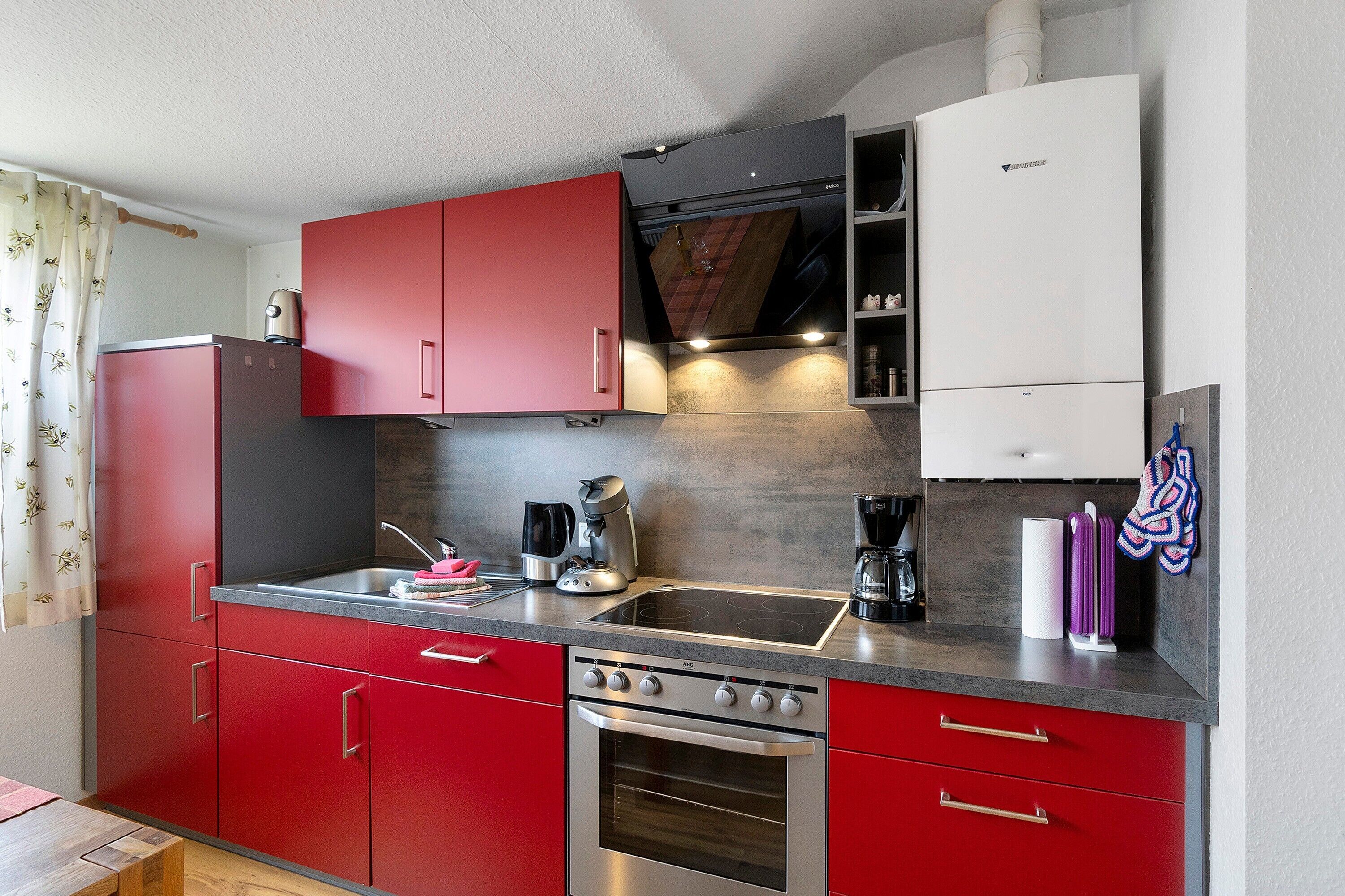 A compact kitchen with red cabinets, a stainless steel sink, and a built-in oven.