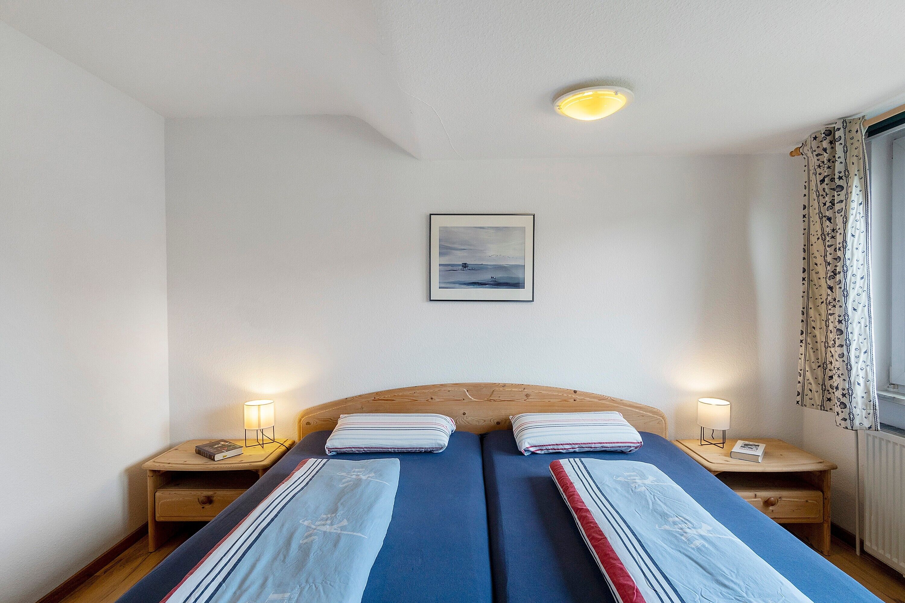 Ein Schlafzimmer mit zwei Betten, einem gerahmten Bild an der Wand und Nachttischlampen.