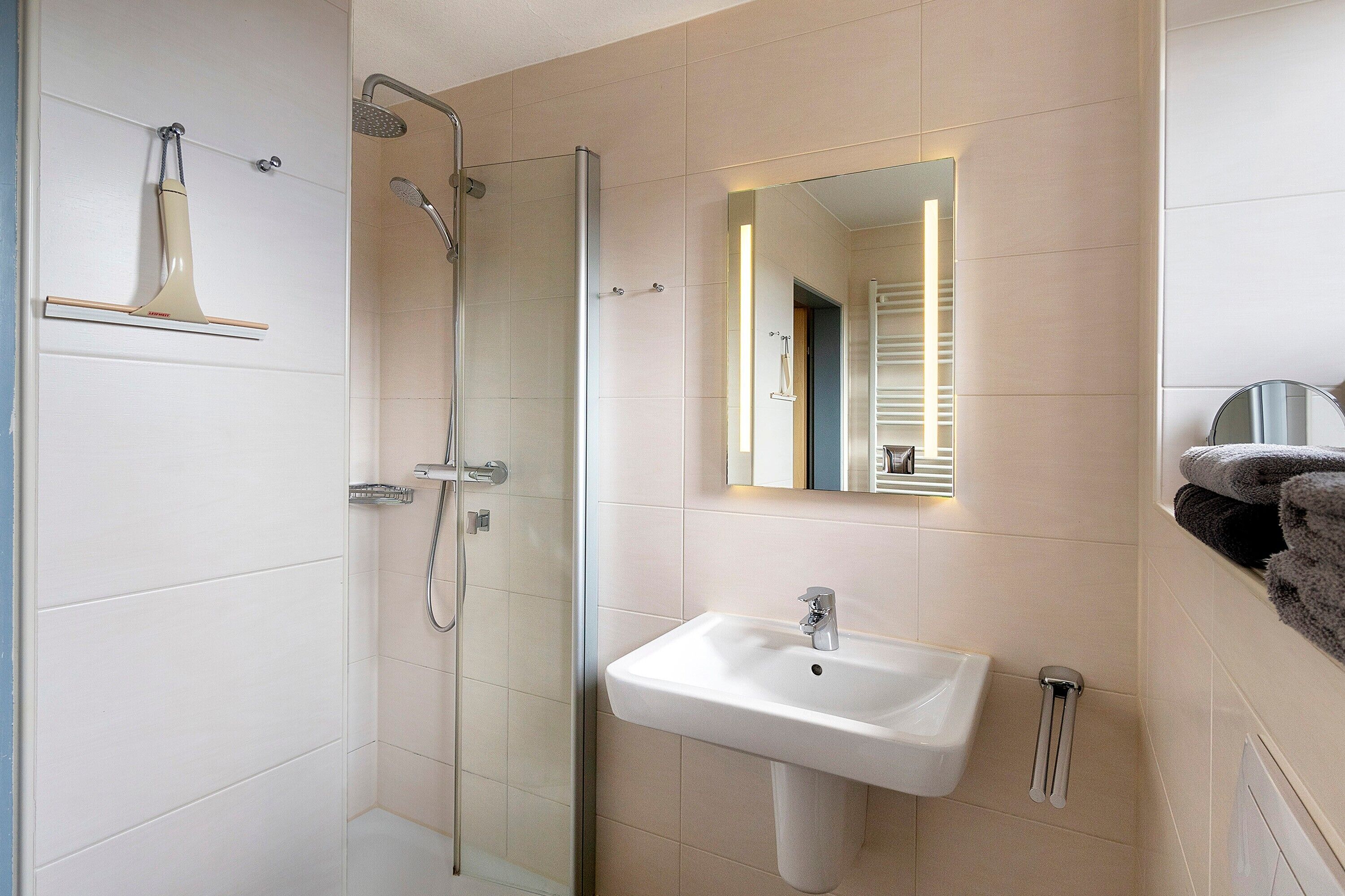 A modern bathroom with a glass shower enclosure, a white sink, and a mirror with a lighted frame.