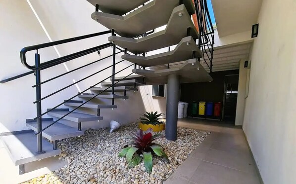 A modern outdoor staircase with metal railings, surrounded by pebbles and potted plants.